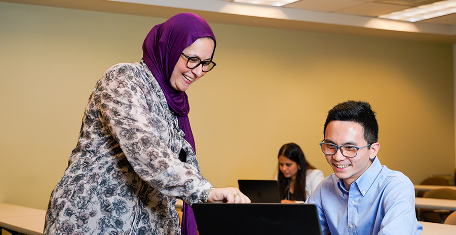 A faculty member and student look at a laptop together in a classroom